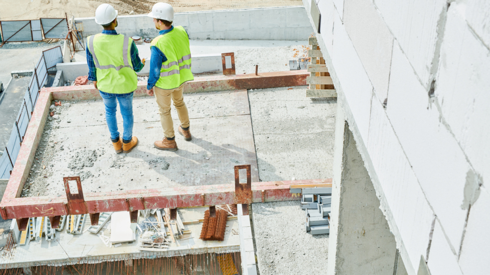 Rear view of contemplative modern constructors in safety vests and hardhats working on new house and discussing building process